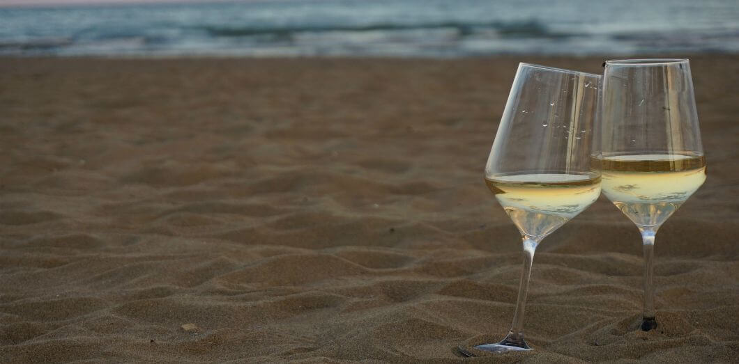 deux verres de vin blancs sur une plage au soleil couchant